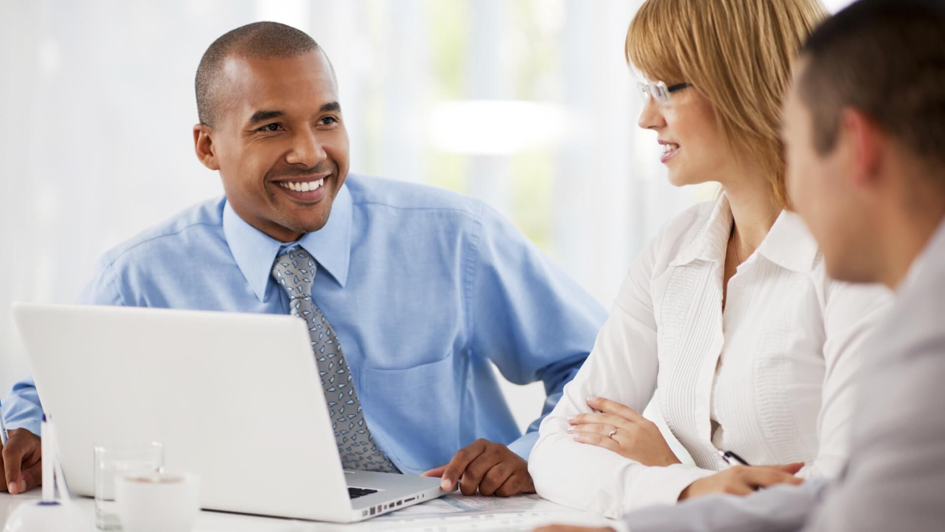 Man with laptop smiling facing two people