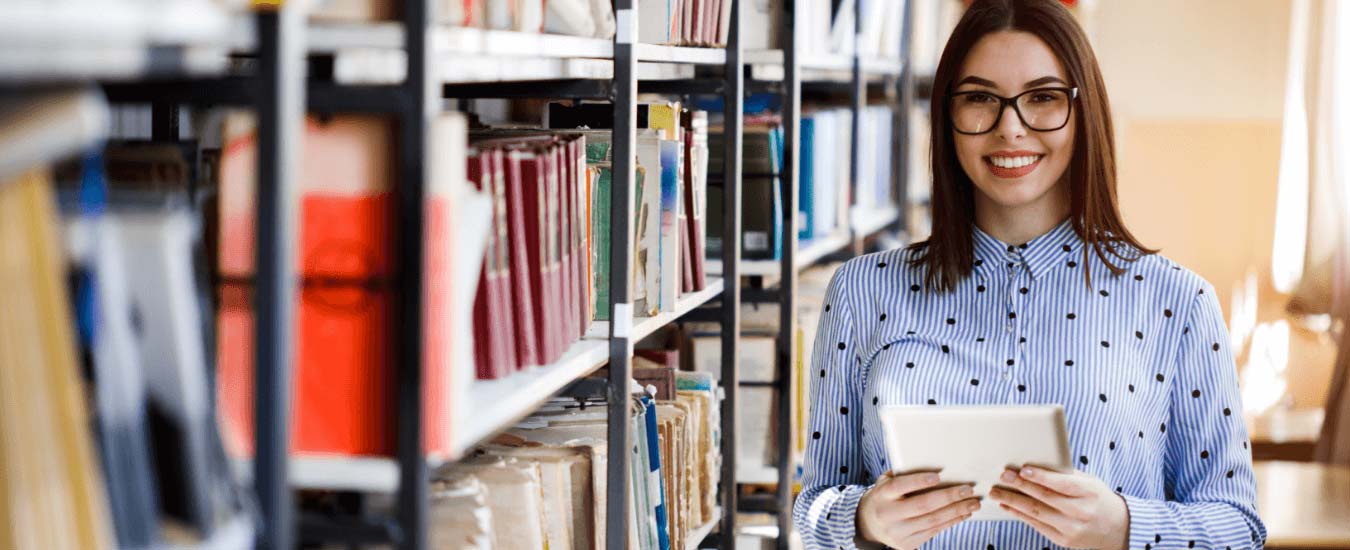 Library Staff Smiles Besides A Bookshelf